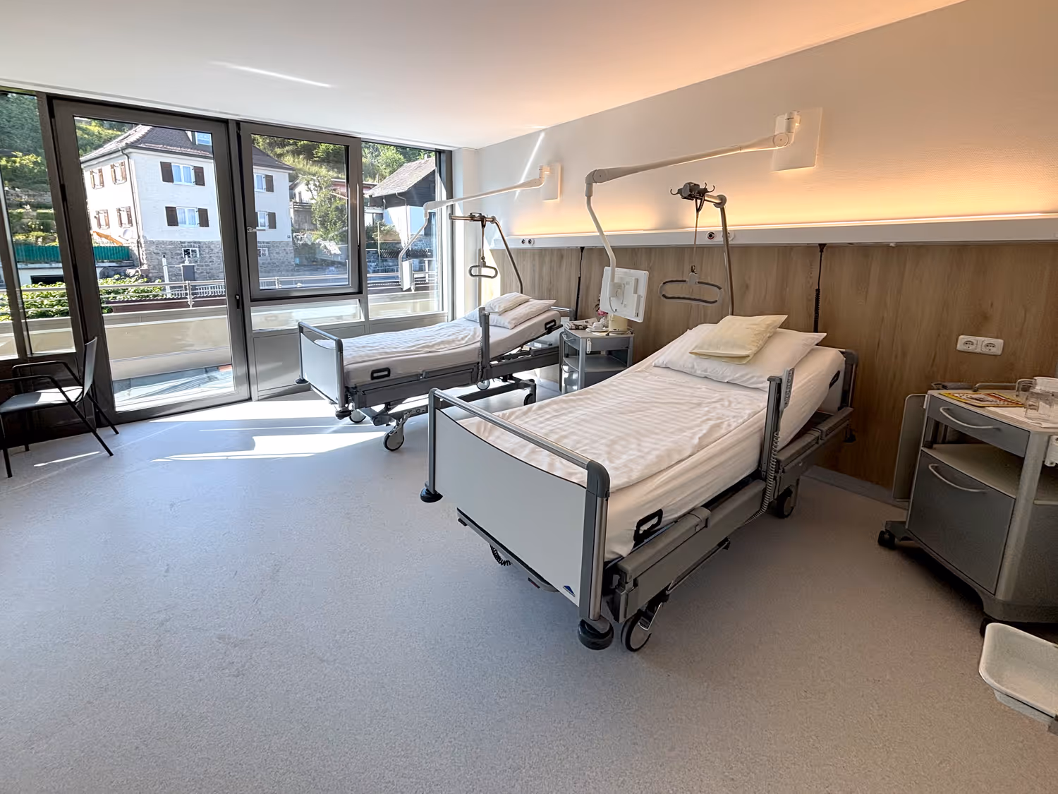Modernes Klinikum mit zwei Betten und großem Fenster mit Blick auf Häuser und Grünfläche.