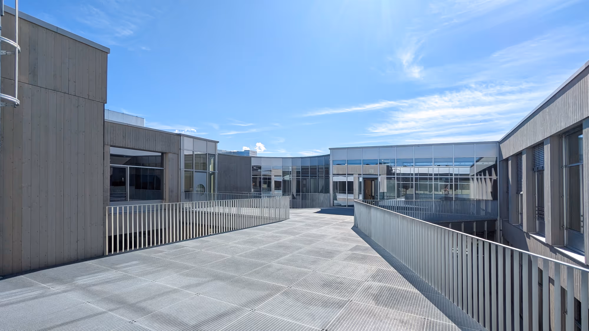 Moderner Gebäudekomplex einer Werkstatt mit großen Fenstern und einer breiten, erhöhten Metallplattform unter blauem Himmel.