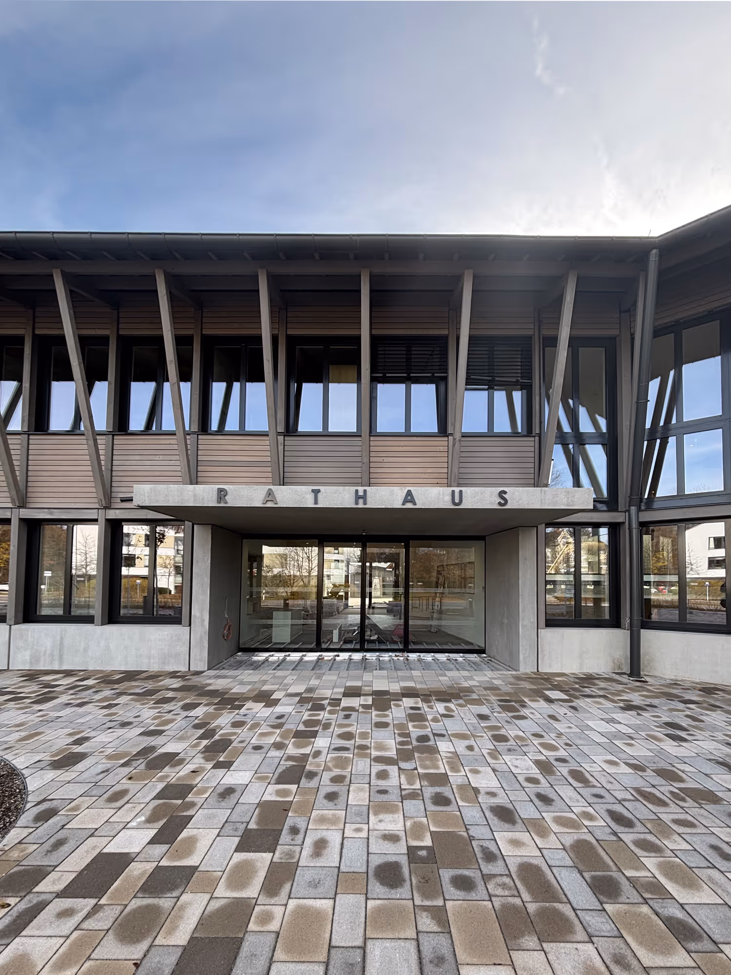 Eingang eines modernen Rathauses mit großen Fenstern und gepflastertem Vorplatz.