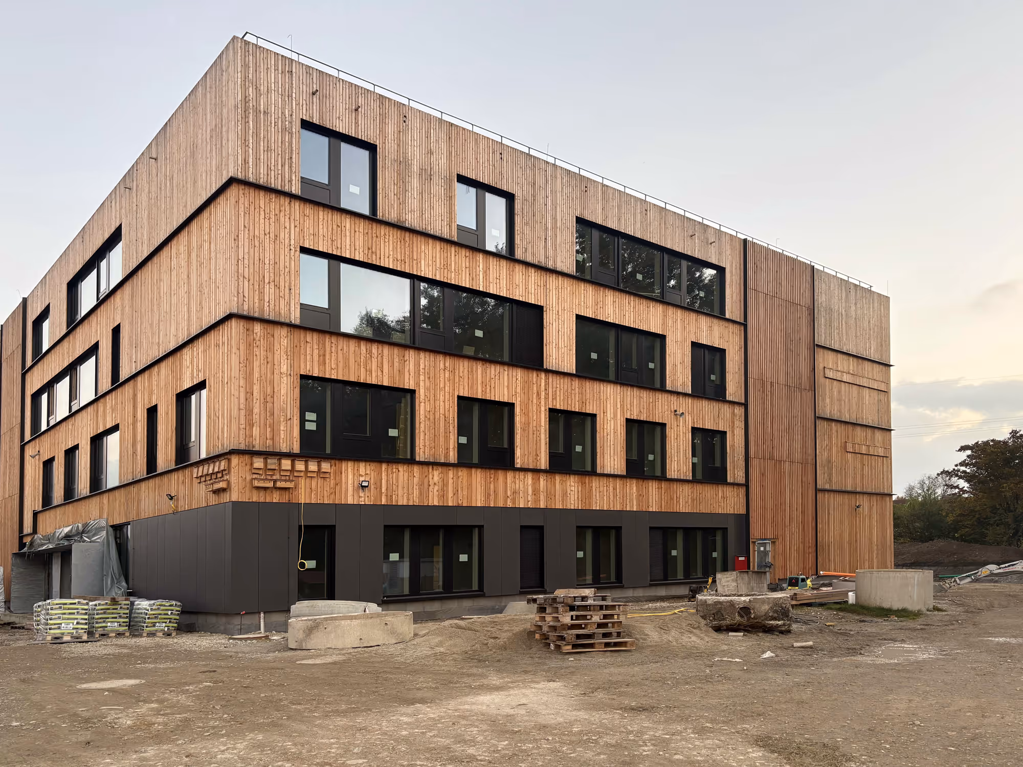 Modernes mehrstöckiges Gebäude mit Holzverkleidung und großen Fenstern auf einer Baustelle.