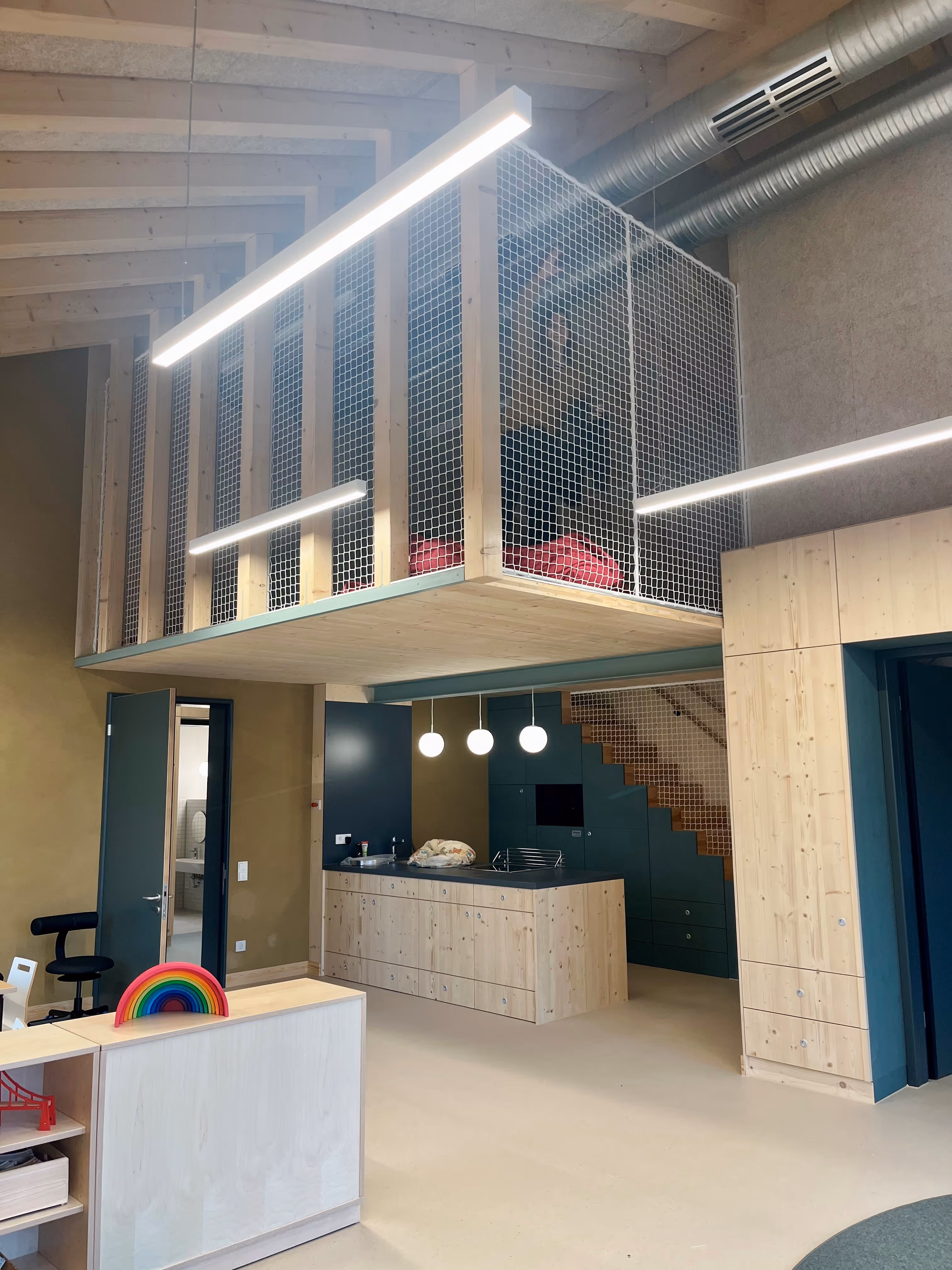 Moderner Innenraum mit Holzloft, Netzgeländer und heller Einrichtung mit Küche und Treppe.