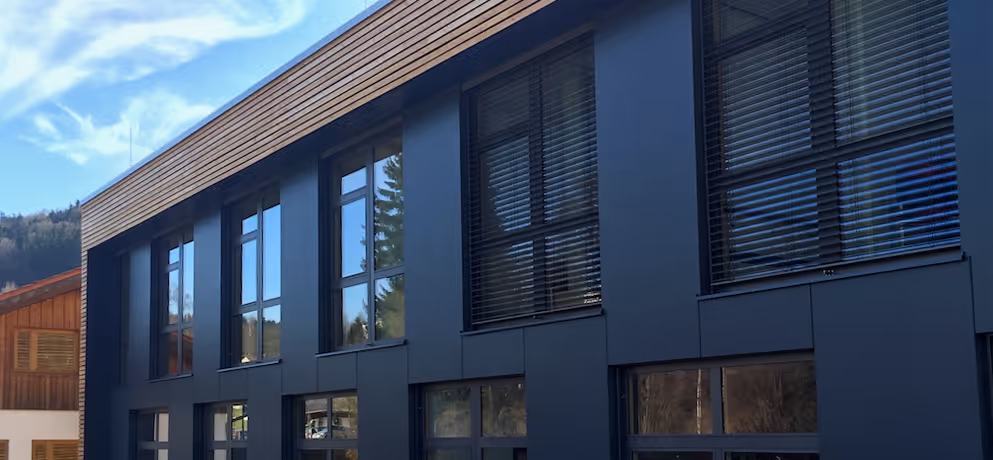 Modernes Gebäude mit dunkler Fassade und großflächigen Fenstern unter blauem Himmel mit einigen Wolken.