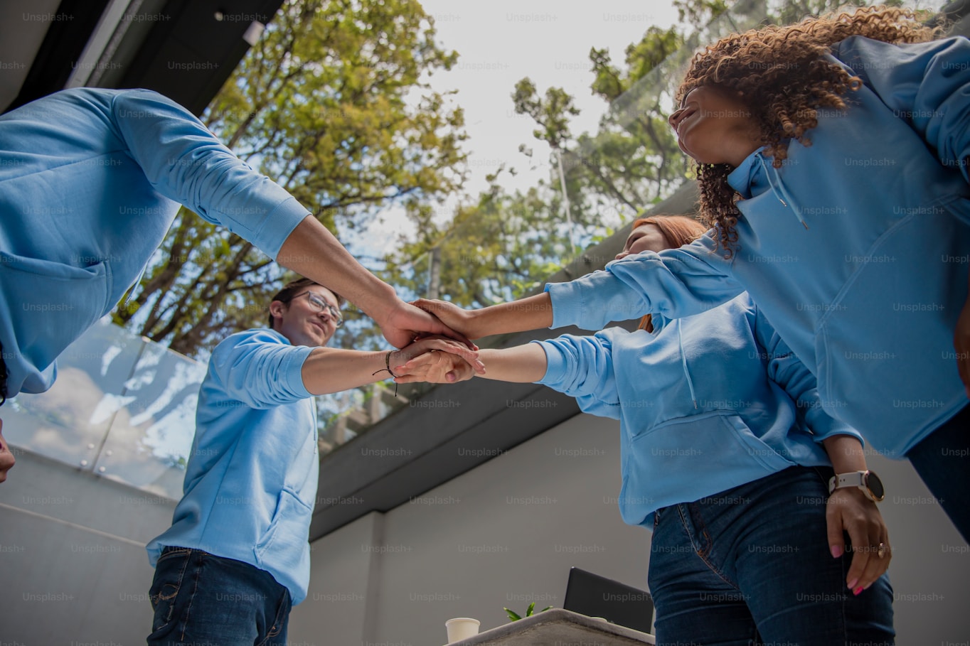Teammates in blue shirts joining hands in teamwork and unity outdoors