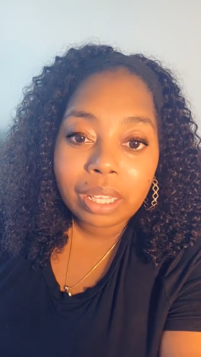 Smiling young woman with curly hair wearing black shirt and gold jewelry