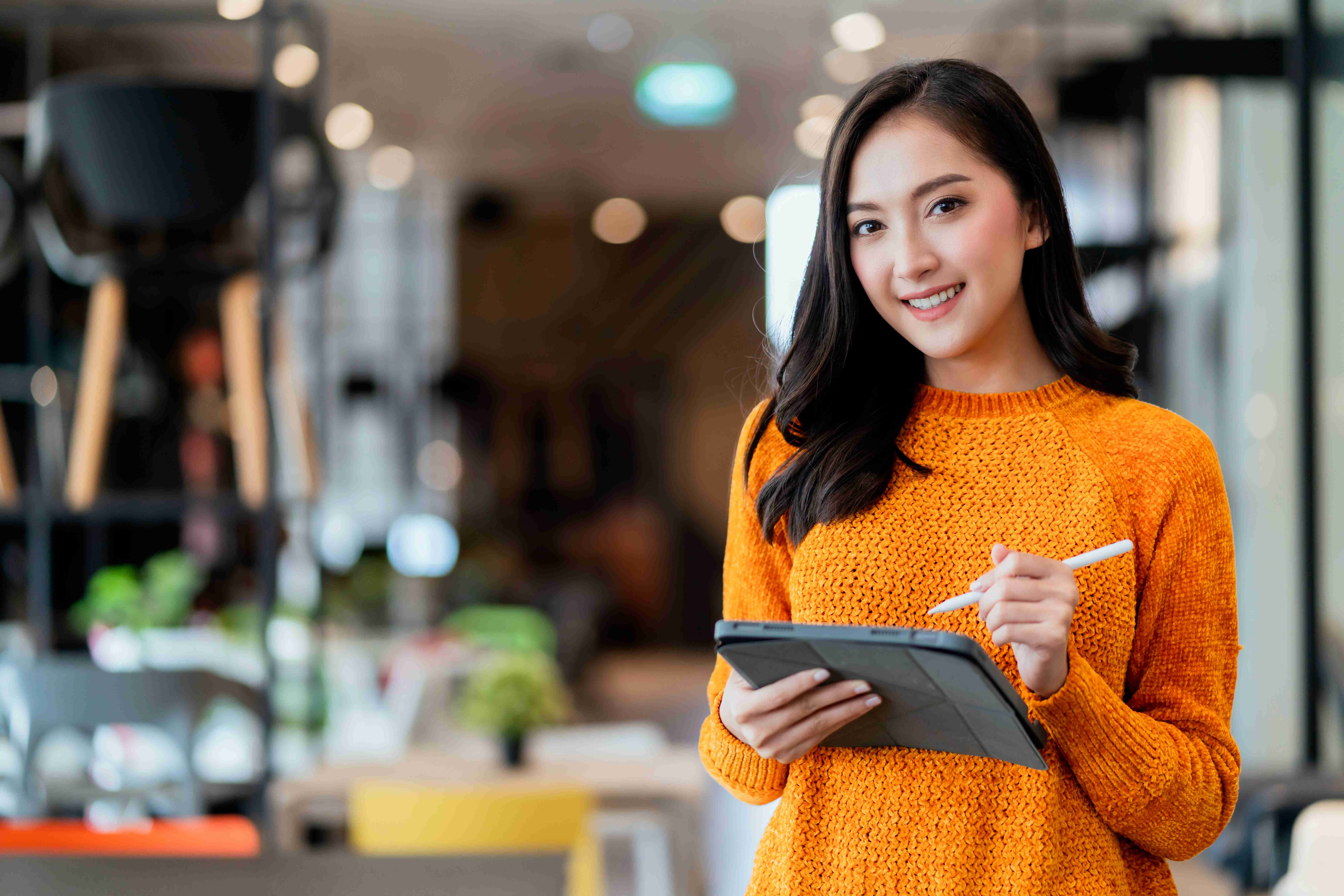 Smiling woman in orange sweater using tablet in modern office