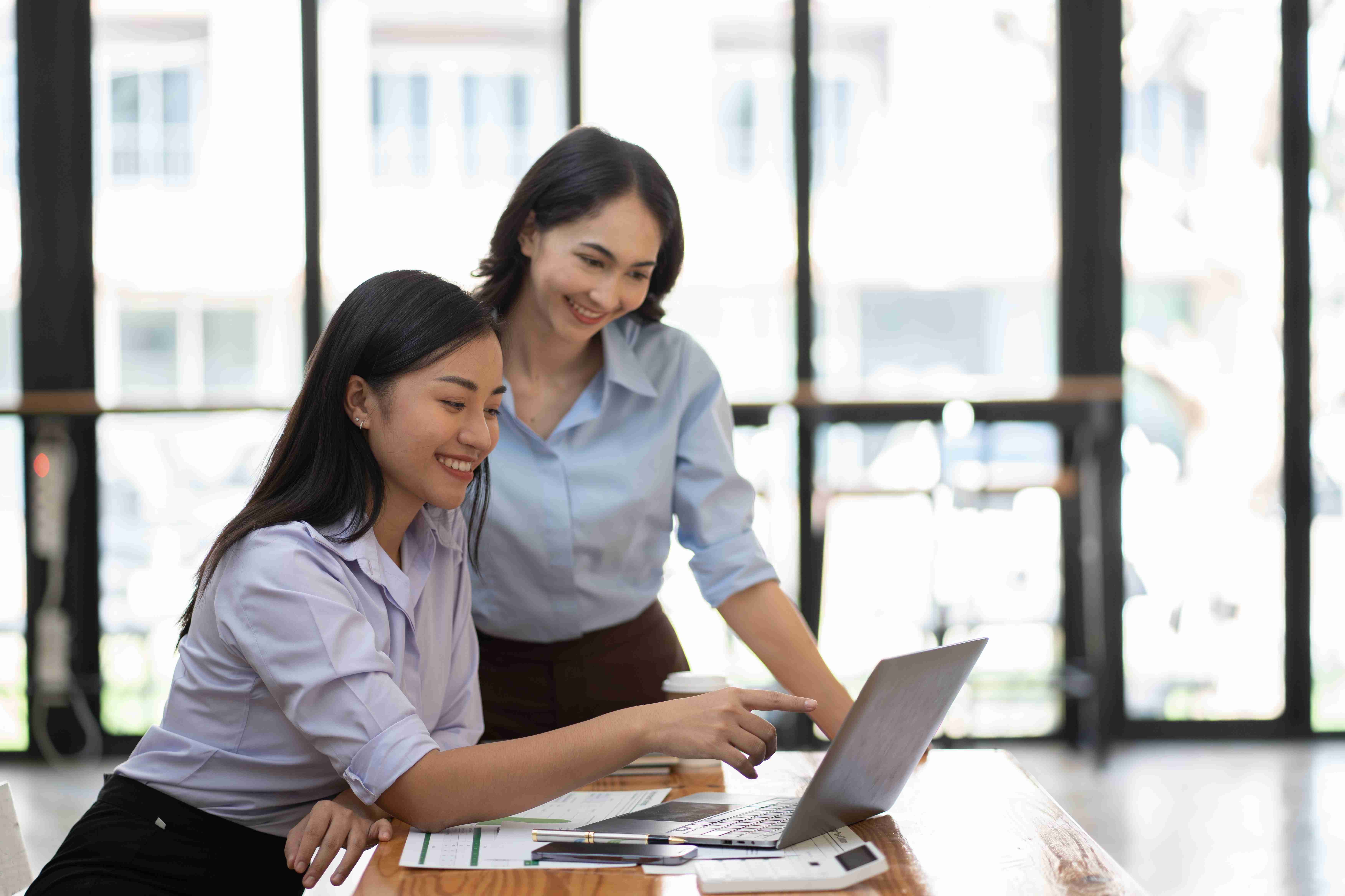 Two women collaborating on a laptop in a bright office workspace
