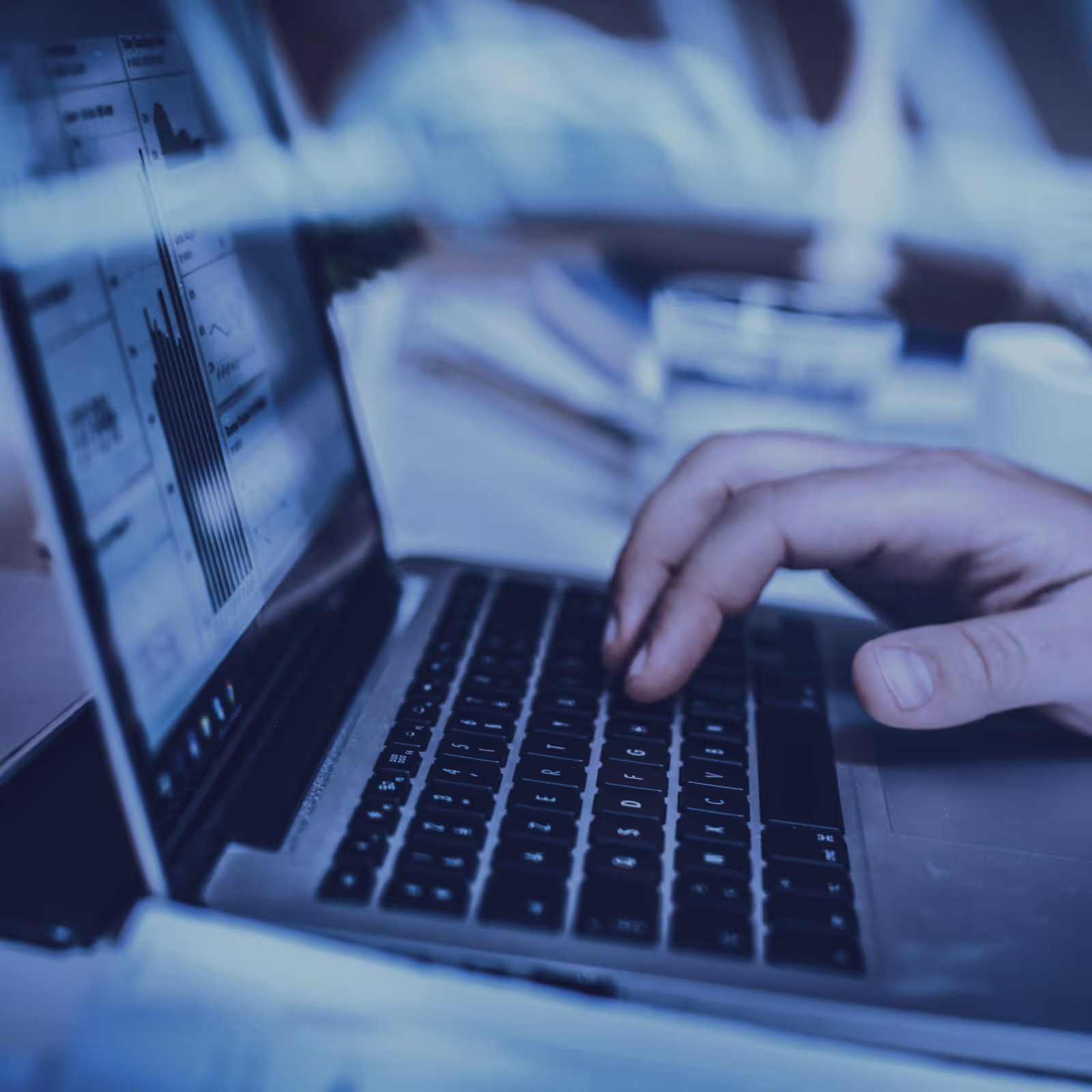 Person's hand typing on a laptop keyboard with data charts displayed on the screen.
