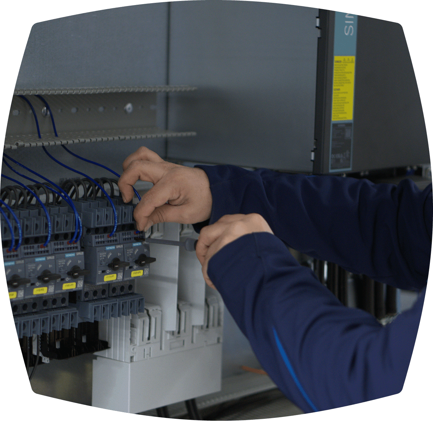 Elektrikerhände montieren Kabel in einem Schaltschrank mit Schutzschaltern, farbigen Drähten und Klemmenleisten.