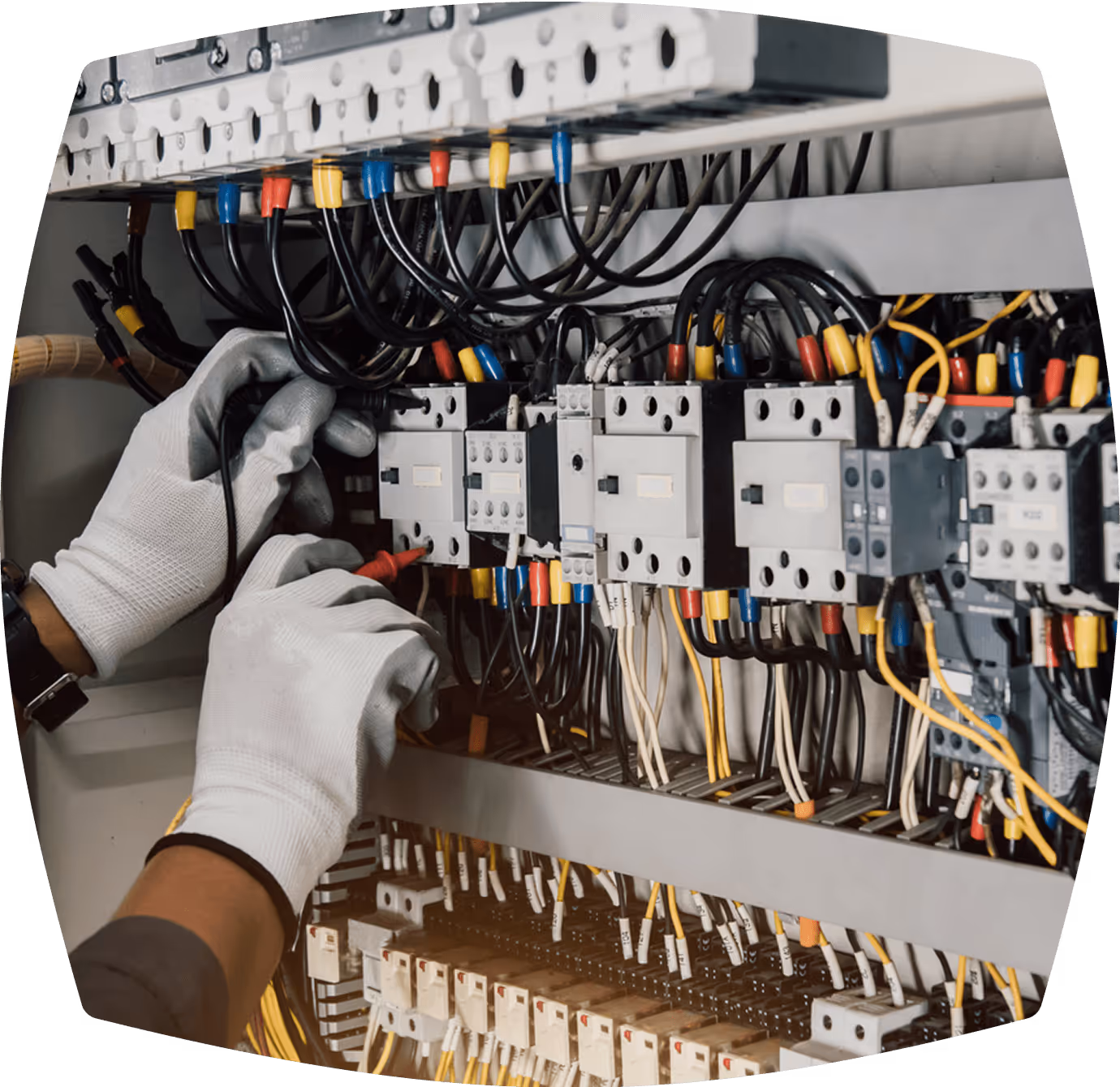 Elektrikerhände montieren Kabel in einem Schaltschrank mit Schutzschaltern, farbigen Drähten und Klemmenleisten.