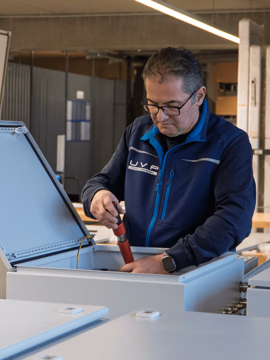 Mann im blauen Arbeitsanzug repariert elektrischen Schaltschrank in Werkstatt.