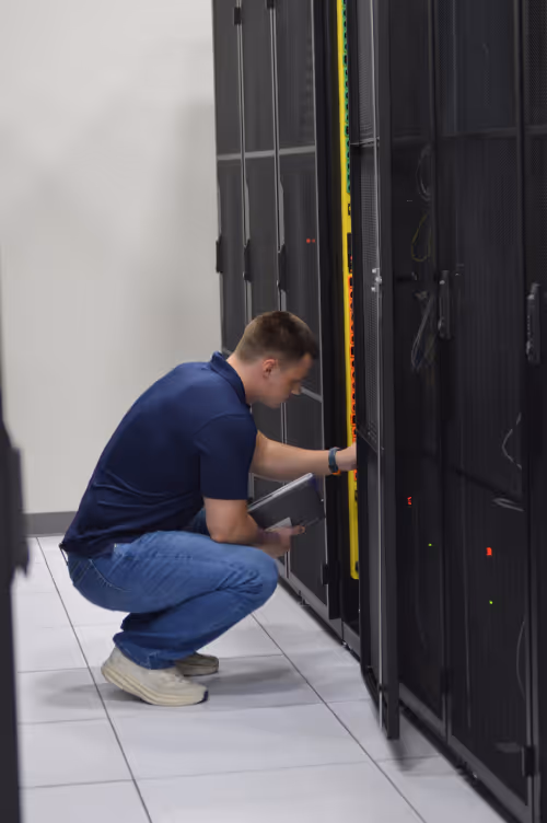 IT technician crouching to install or inspect server rack equipment in a professional data center