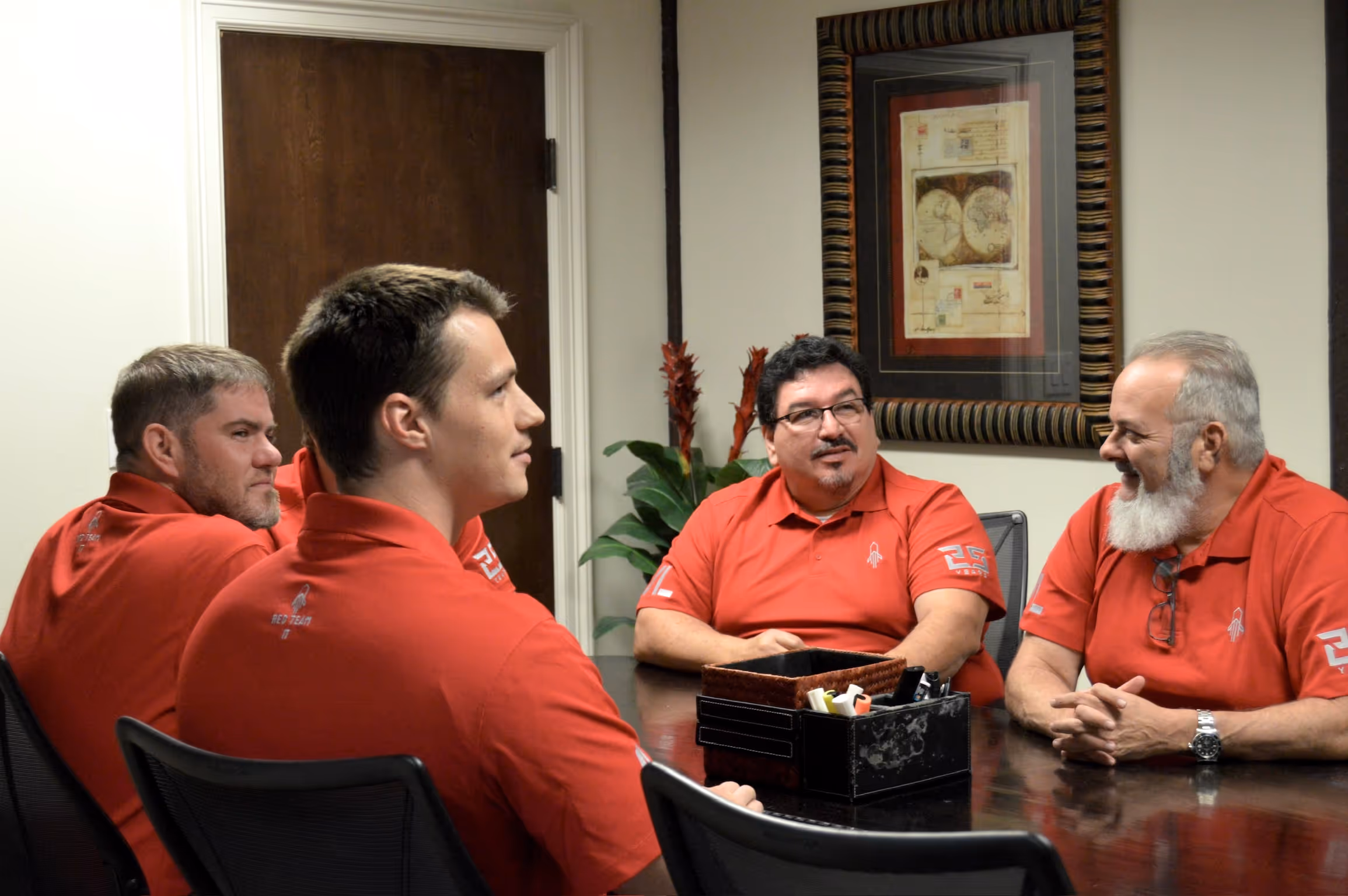 Red Team IT managed services team meeting in conference room, four professionals in red polo shirts discussing IT solutions