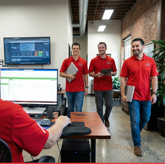 Red Team IT technicians in red polo shirts walking through modern office carrying laptops and tablets