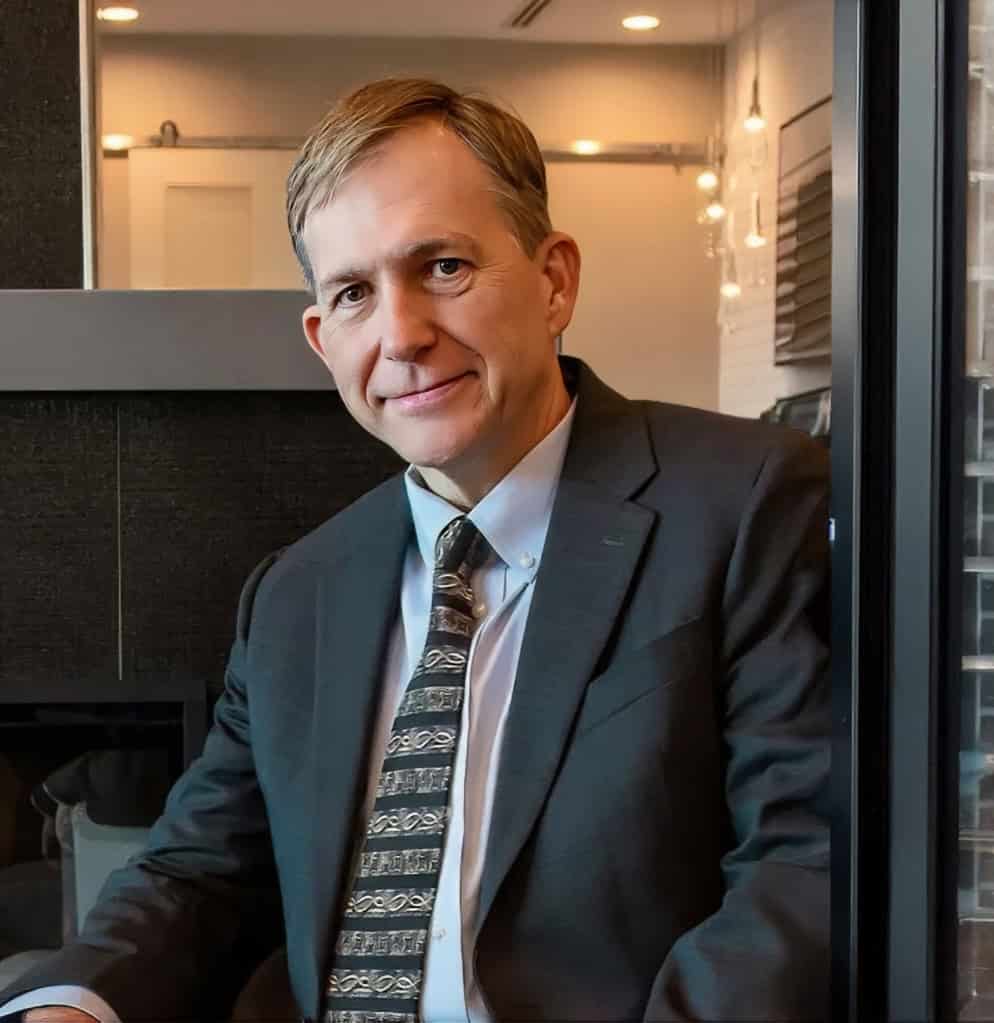 Professional IT consultant in suit and tie seated in modern office, smiling confidently at camera