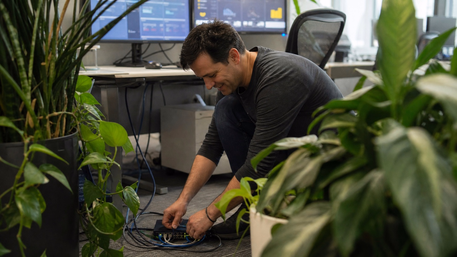Man on floor connecting network cables near desk plants