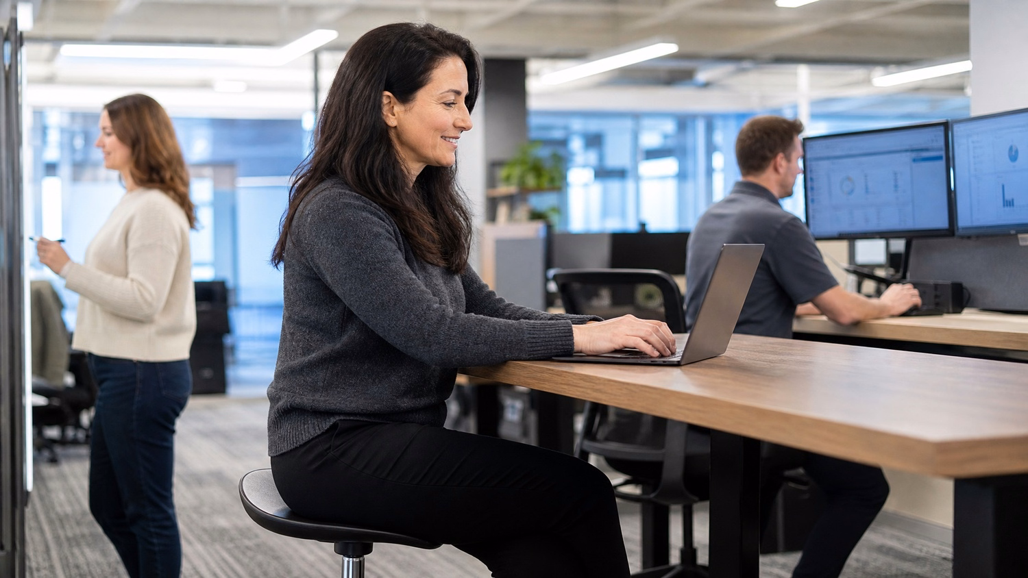 Woman on stool desk types on laptop, nonprofit tech