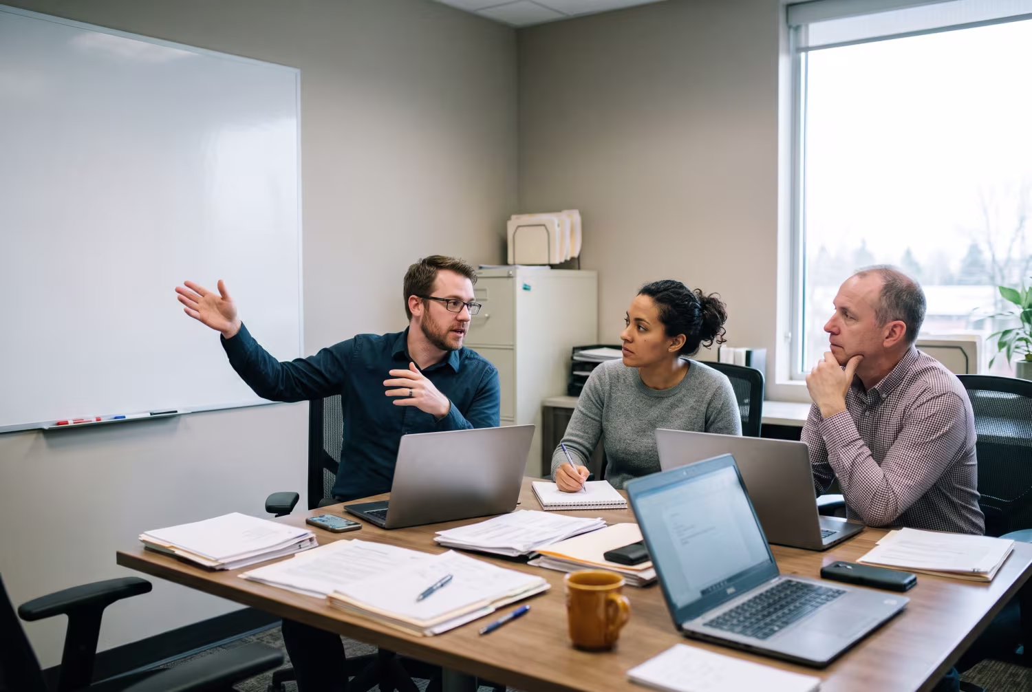 Three IT professionals discussing around a cluttered conference table