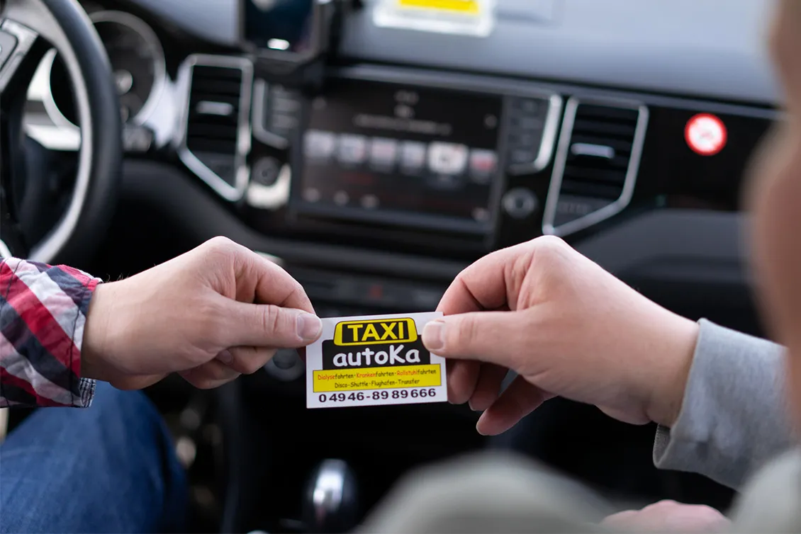 Zwei Hände tauschen eine Taxi-Visitenkarte im Innenraum eines Autos aus.
