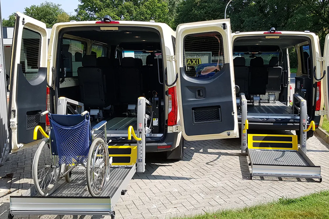 Zwei behindertengerechte Kleinbusse mit geöffneten Hecktüren, rechte Ladefläche mit Rollstuhl und Hebebühnen für barrierefreien Zugang.