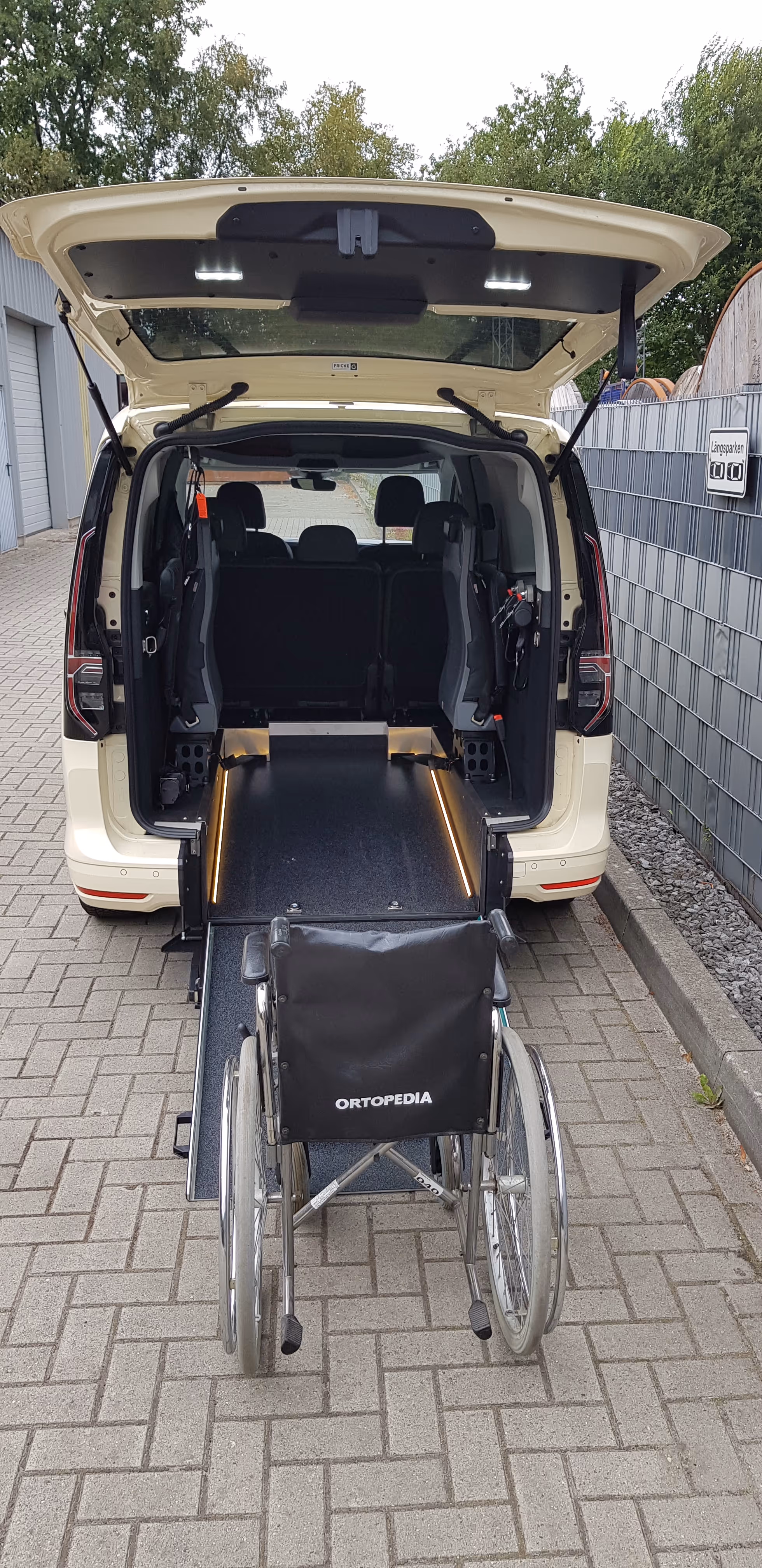 Rollstuhl vor einem Van mit offener Heckklappe und ausgefahrenem Rampe für Barrierefreiheit.
