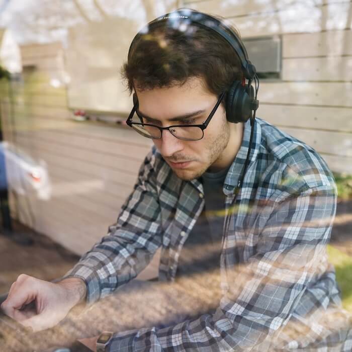 Junger Mann mit Brille und Kopfhörern, der an einem Mischpult arbeitet, draußen hinter einer Fensterscheibe.