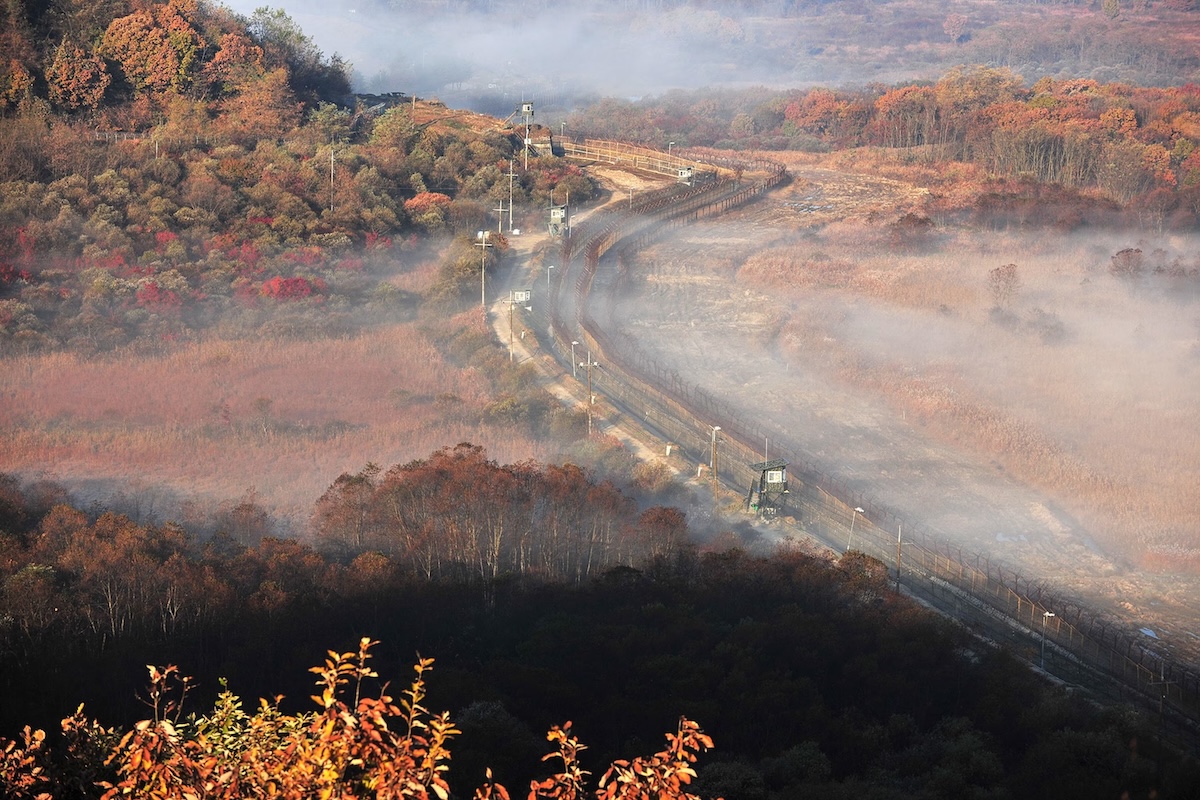 Barbed-wire fences and guard towers cut through autumn foliage and morning mist along the southern edge of the Korean Demilitarized Zone.