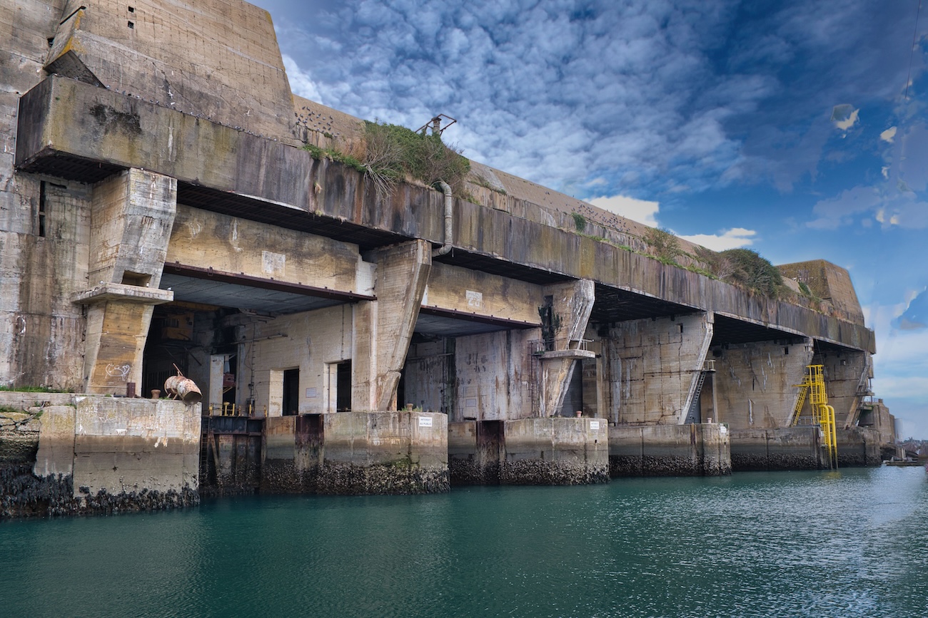 Keroman submarine base in Lorient, France, seen from the water, with open concrete U-boat pen entrances beneath the bunker's overhanging reinforced roof.