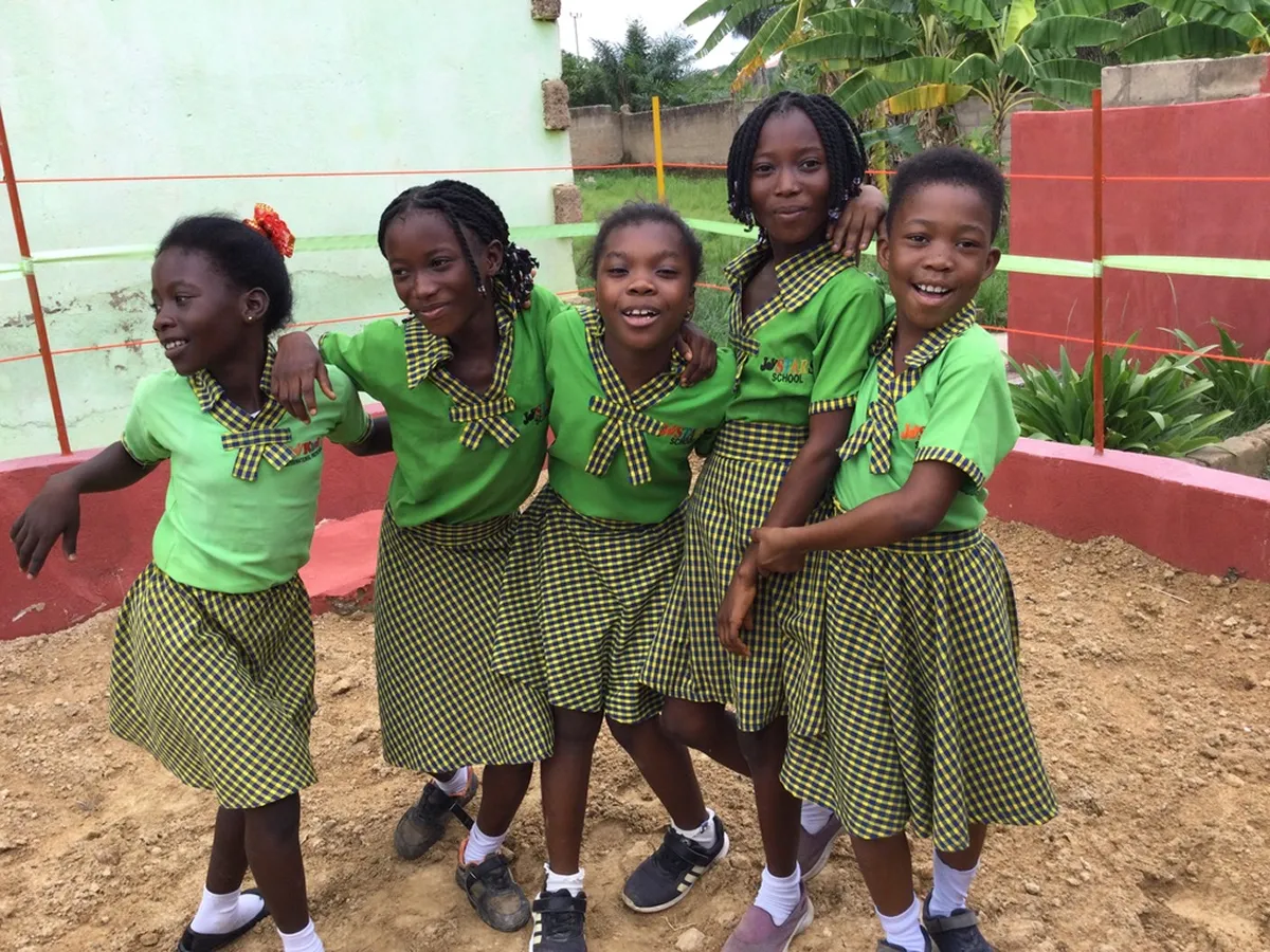 Fünf Mädchen in grünen Schuluniformen umarmen sich und lachen auf dem Schulhof