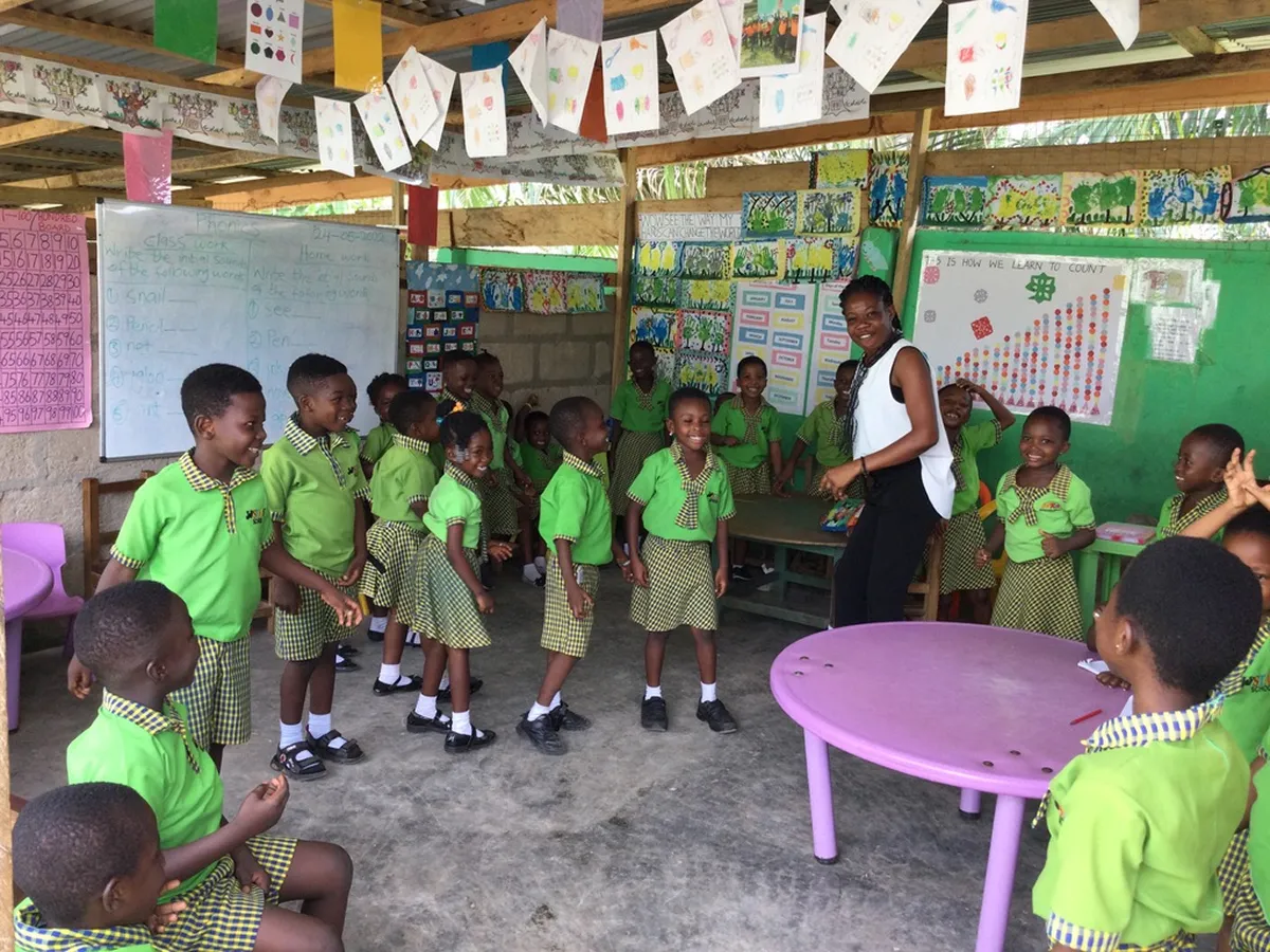 Schulkinder in grüner Uniform mit Lehrerin in einem bunt dekorierten Klassenzimmer in Ghana