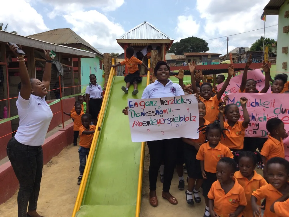 Kinder und Lehrerinnen mit Dankesplakaten neben einer grünen Rutsche auf dem Abenteuerspielplatz
