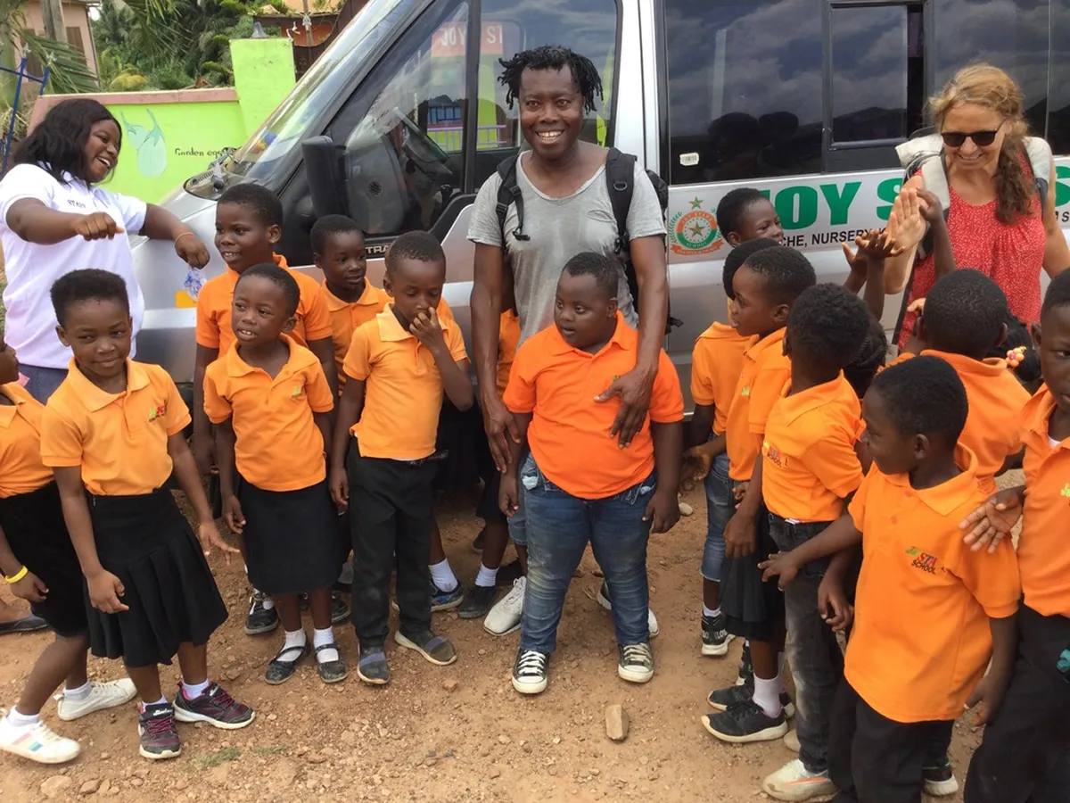 Gruppe von Schulkindern in orangefarbenen Uniformen vor einem Kleinbus, begleitet von Erwachsenen in Ghana