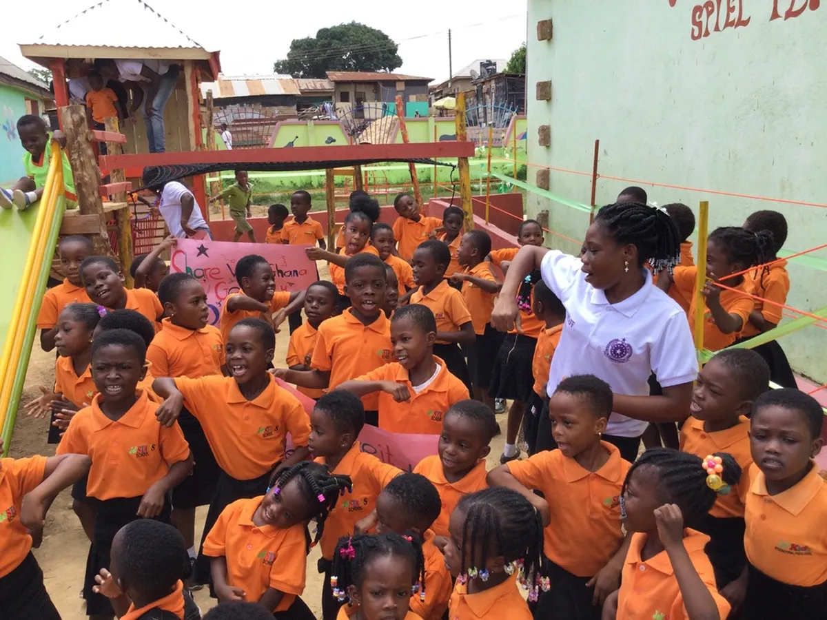 Gruppe von Schulkindern in orangefarbenen Uniformen spielt und tanzt fröhlich auf dem Schulhof in Ghana
