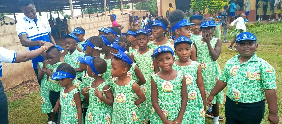 Kinder in grüner Schuluniform mit blauen Kappen bei einer Feier in Ghana