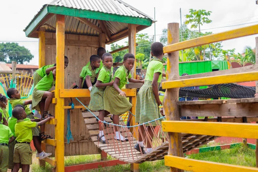 Kinder in Schuluniform klettern und laufen über eine Holzbrücke auf dem Spielplatz in Ghana