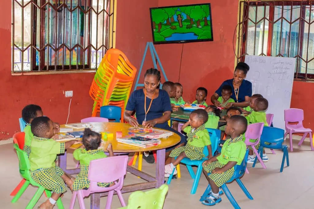 Lehrerin unterrichtet kleine Kinder in grünen Schuluniformen in einem Klassenraum der Joy Stars School in Ghana