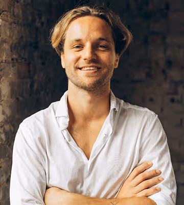 Lächelnder Mann in weißem Hemd vor Ziegelwand.