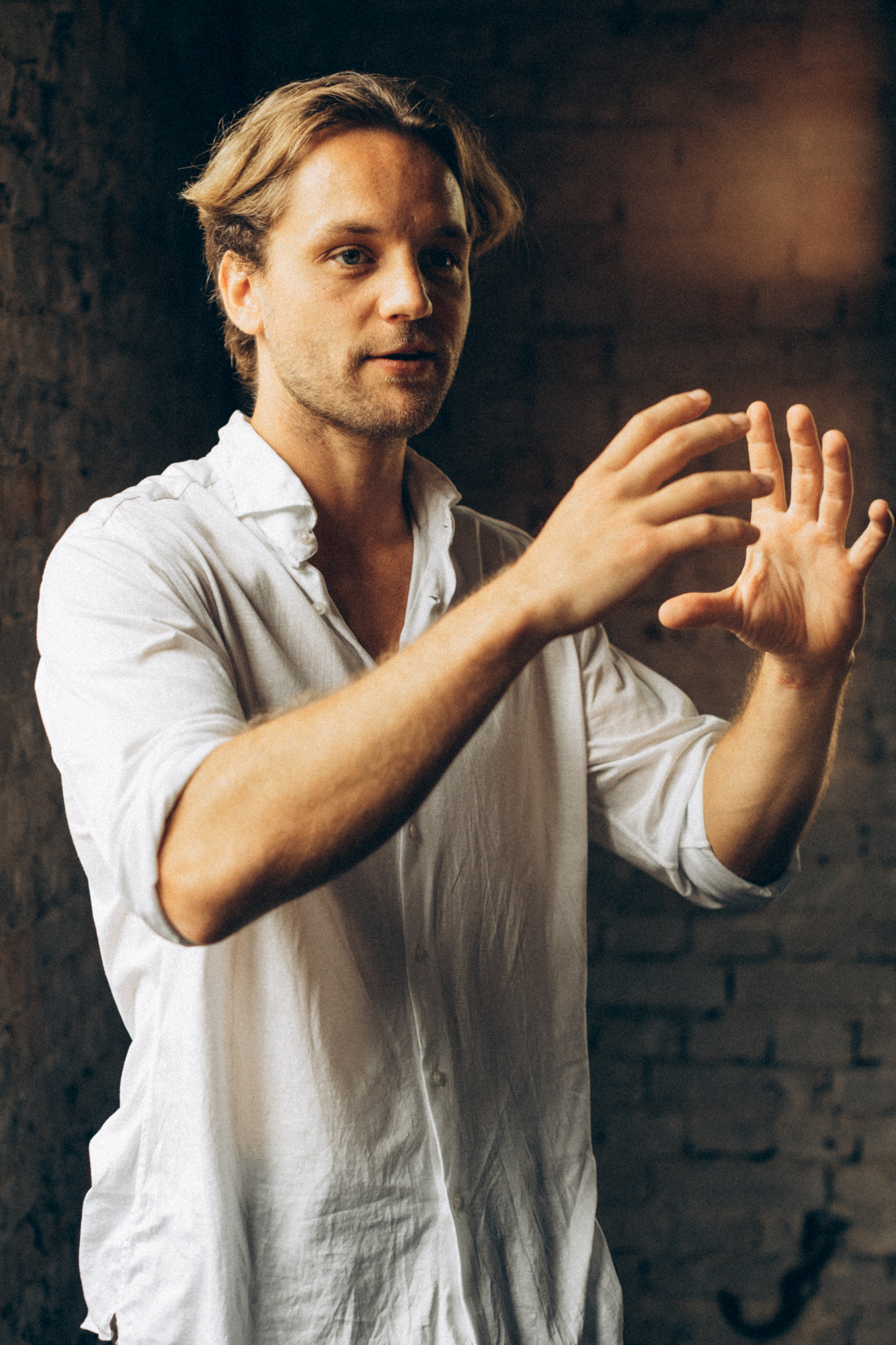 Lächelnder Mann in weißem Hemd, vor einer Backsteinmauer, mit verschränkten Armen.