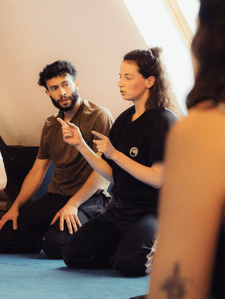 Trainerin erklärt eine Übung während einer Movement-Session, Teilnehmende hören aufmerksam zu.