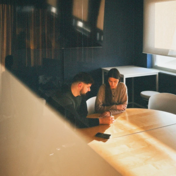 Two people sitting at a wooden table in a softly lit room, engaged in conversation.