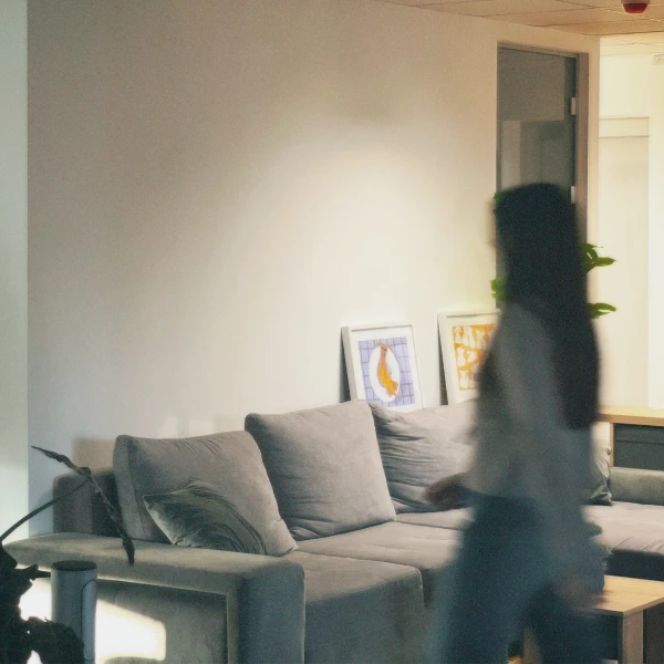 Blurred woman walking past a gray couch with artwork on the wall in a modern living room.