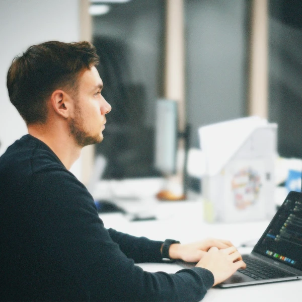 Young man with short hair and beard typing on a laptop in a modern office setting.