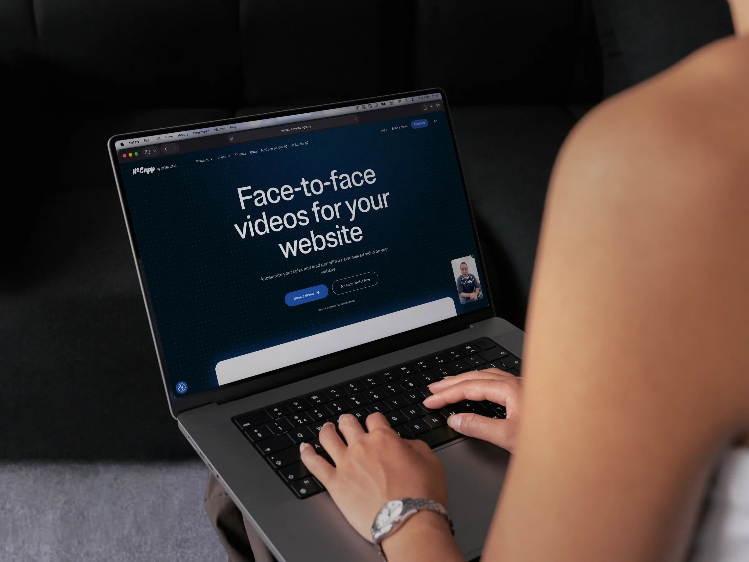 Over-the-shoulder view of a person typing on a MacBook laptop displaying the 'NoCapp' website homepage, featuring the headline 'Face-to-face videos for your website' and a video widget in the corner.