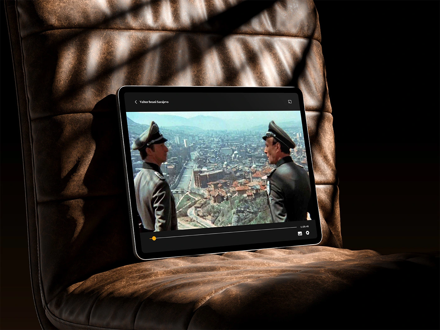 A tablet device resting on a brown leather chair, displaying a streaming video interface playing a scene from the movie 'Valter brani Sarajevo'