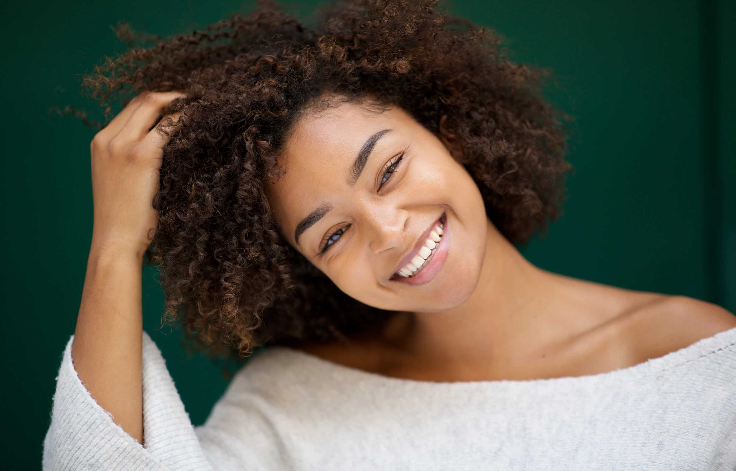 A woman smiling, touching her hair