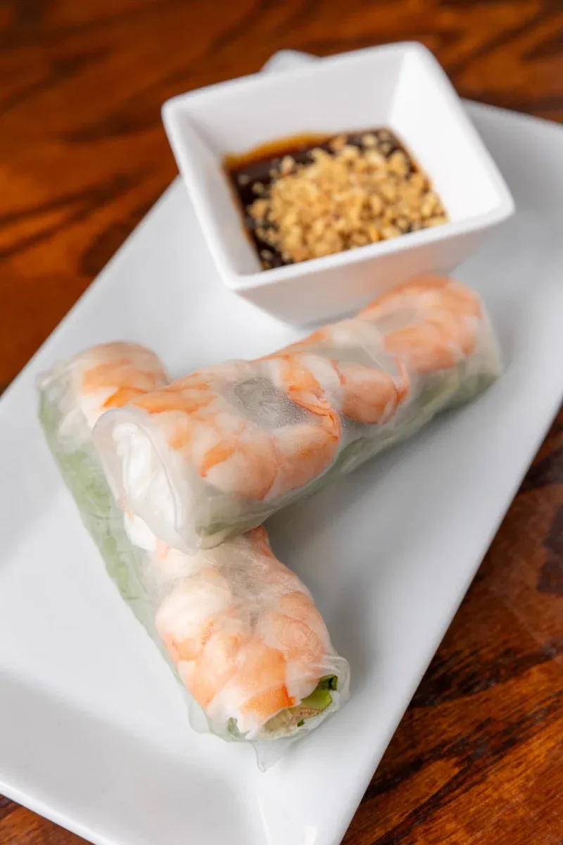 Fresh shrimp spring rolls served with a small bowl of dipping sauce on a white plate.