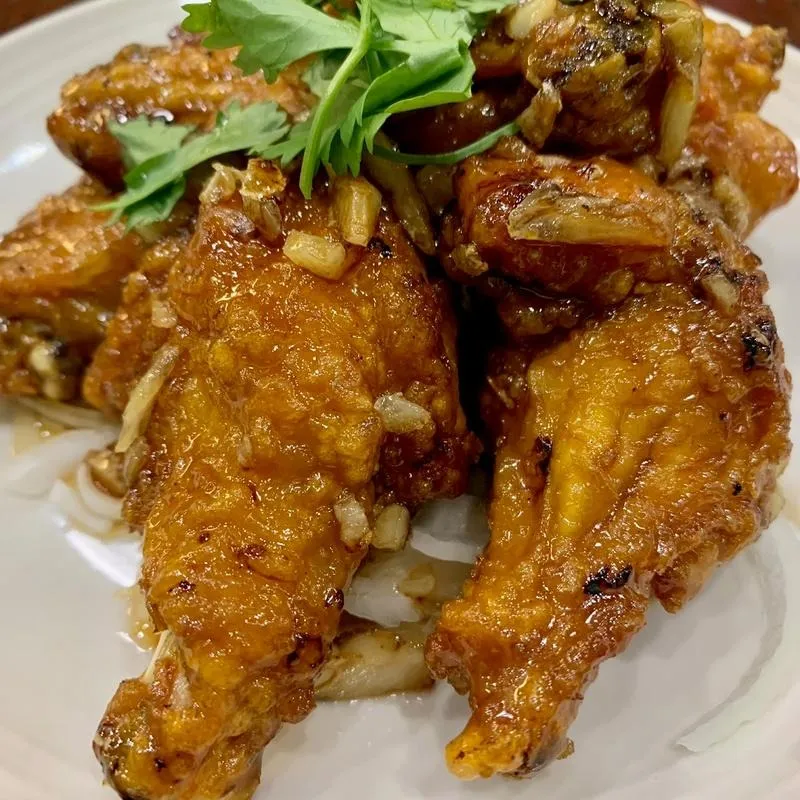 A white plate holds chicken wings drizzled with sauce and topped with fresh garnish.
