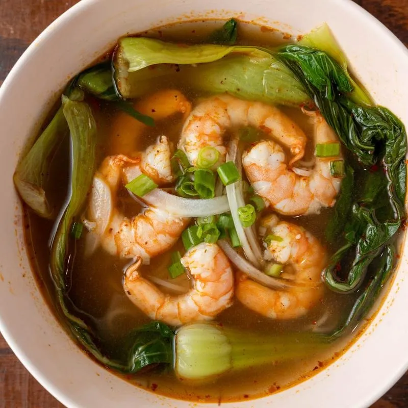 A bowl of soup filled with shrimp and colorful vegetables, garnished for a vibrant presentation.