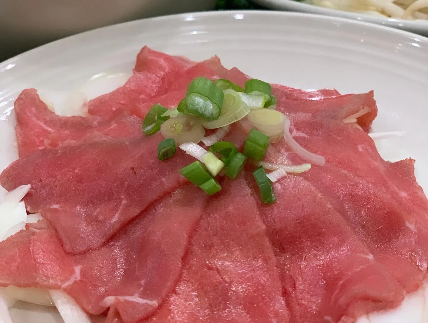 A plate of cooked meat garnished with fresh green onions.