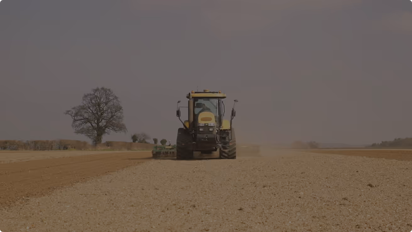 Tractor tilling soil in a large open field under a cloudy sky.