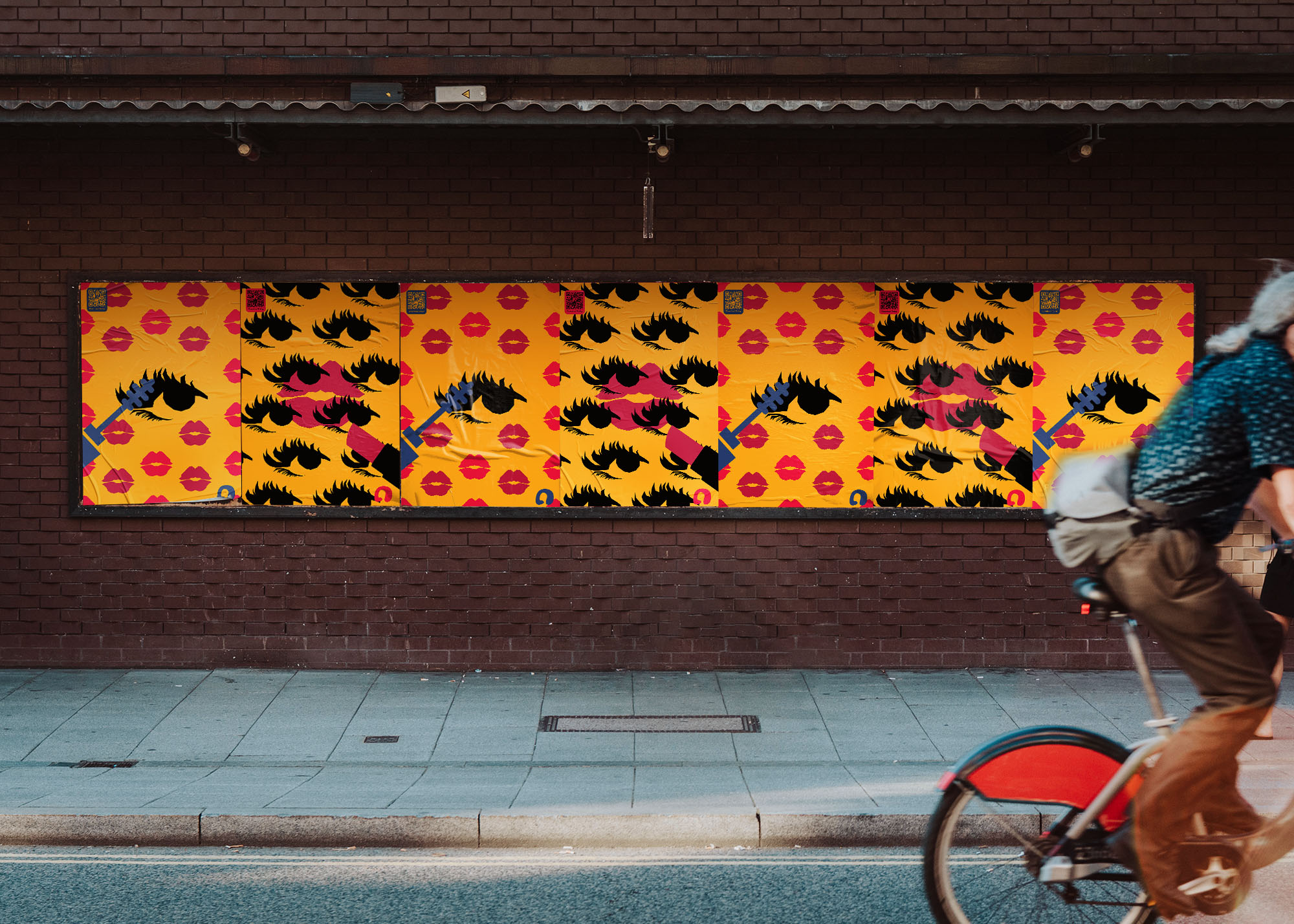Colorful street art posters with black eyelashes and red lipstick marks on yellow background on a brick wall, with a cyclist passing by in the foreground.